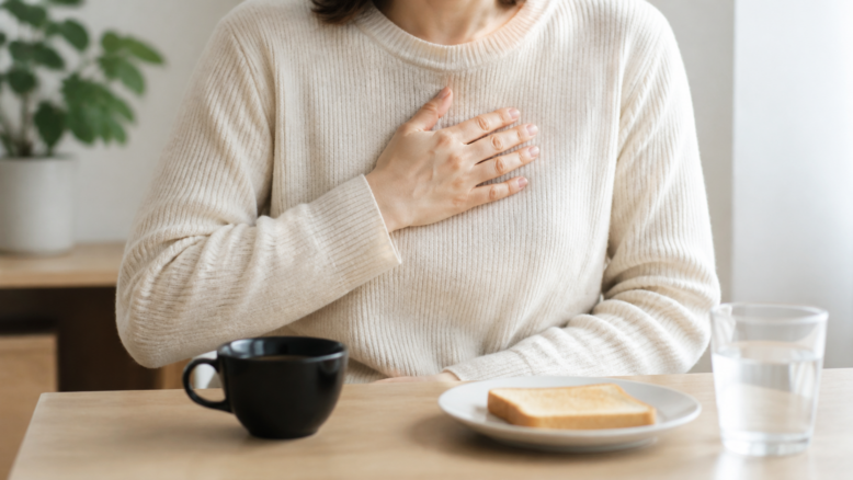 Person mit Sodbrennen vor Kaffee, Toast und Wasser [Bildinhalt mit KI erstellt]